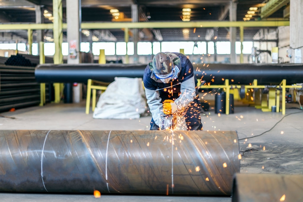 Metal worker in protective suit and gloves cutting pipe with electric grinder
